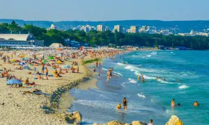 Słoneczna plaża w Bułgarii, idealna na wakacje last minute all inclusive. Tłumy ludzi opalają się i kąpią w morzu.