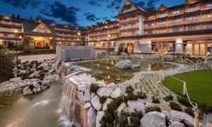 Elegancki hotel z basenami termalnymi, z kaskadą wodną i stawem w otoczeniu kamieni i zieleni.
