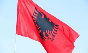 Czerwona flaga Albanii z czarnym dwugłowym orłem powiewa na tle błękitnego nieba. Zastanawiasz się, ile trwa lot do Albanii?