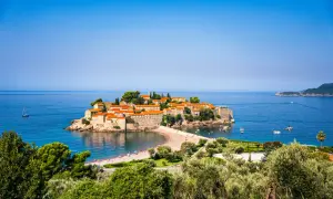Wyspa Sveti Stefan, jedna z głównych atrakcji Budvy, otoczona turkusowym morzem, z piaszczystą plażą i łodziami.