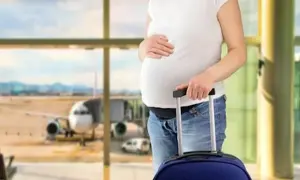 Kobieta w 7 miesiącu ciąży z walizką na lotnisku, gotowa na lot samolotem.