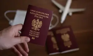 Dłoń trzyma polski paszport. Obok leżą kolejne dokumenty, maseczka i samolot. Zastanawiasz się, ile trwa wyrobienie paszportu?
