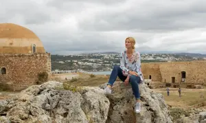 Kobieta siedzi na skale na Krecie. Październikowa temperatura jest przyjemna, w tle widać miasto i zabytkowe budowle.