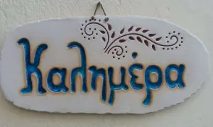 Ceramiczna tabliczka z napisem "Καλημέρα" (do zobaczenia po grecku) i ozdobnym motywem roślinnym.