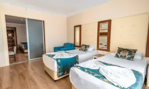 Pokój hotelowy z dwoma łóżkami, ozdobiony turkusowymi narzutami. Widok na sąsiedni pokój przez przesuwne drzwi. Idealne miejsce na relaks po dniu spędzonym w beach club doganay.