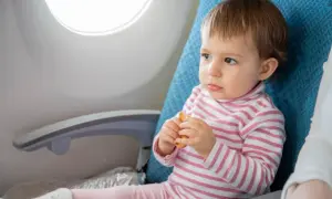 Małe dziecko z zaciekawieniem patrzy przez okno samolotu, trzymając w rączkach ciasteczko. To jego pierwszy lot samolotem z dzieckiem 3 letnim.