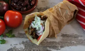 Pyszny pita gyros z mięsem, warzywami i sosem, obok pomidory, oliwki i cebula.