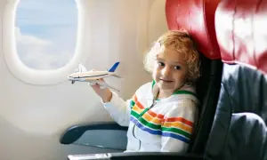 Chłopiec z blond kręconymi włosami bawi się modelem samolotu w trakcie latania samolotem.