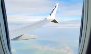 Widok z okna samolotu Ryanair, idealny do nauki, jak szukać tanich wakacji. Podróż nad zielonymi polami i chmurami.