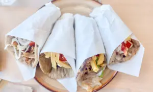 Cztery pyszne souvlaki gyros z mięsem, frytkami, warzywami i sosem, zawinięte w papier, na talerzu.