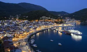 Widok na oświetlone miasto Parga nad morzem o zmierzchu, z górami w tle.