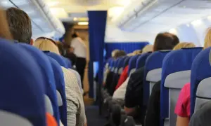 Widok z perspektywy pasażera w samolocie. Siedzący ludzie, niebieskie siedzenia, stewardessa w tle. To może być inspiracja, jak nie bać się latać.