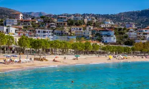Albania, październik: słoneczna plaża z turkusową wodą, zielonymi drzewami i białymi budynkami na wzgórzu.