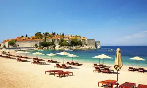Idealne czarnogóra wakacje all inclusive: piaszczysta plaża, leżaki, parasole i widok na urokliwe miasteczko na wyspie.