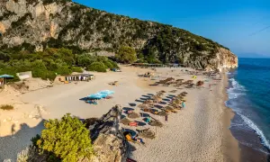 Piękne albania plaże piaszczyste z rzędami parasoli i leżaków, w cieniu skalistego klifu.