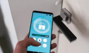Dłoń trzyma smartfon z aplikacją do zdalnego sterowania zamkiem. Ułatwia to samoobsługowy self check-in.