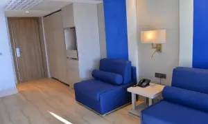 Pokój hotelowy z niebieskimi sofami, drewnianymi meblami i drzwiami. Czuć tu **liberty lykia**, wolność i przestrzeń.