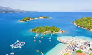 Malownicze **albania morze** z zielonymi wysepkami, plażą z leżakami i wodnym placem zabaw.