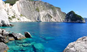 Błękitna woda i białe klify tworzą jedne z najpiękniejszych miejsc na Zakynthos. Ktoś pływa w krystalicznie czystej zatoce.