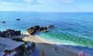Albania, luty. Słoneczna pogoda nad turkusowym morzem, pusta plaża z leżakami i parasolami, łodzie na wodzie.