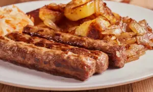 Trzy soczyste ćevapi, klasyka kuchni czarnogórskiej, podane z pieczonymi ziemniakami i cebulą oraz surówką.