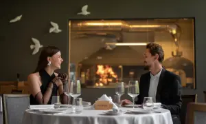Elegancka para cieszy się romantyczną kolacją w restauracji a la carte all inclusive. Za nimi widać kuchnię z ogniem w piecu.