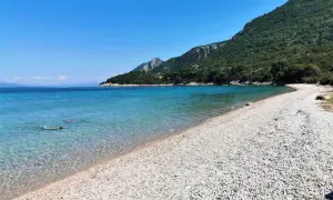 Chorwacja piaszczyste plaże blisko Polski. Dwie osoby pływają w krystalicznie czystej wodzie przy kamienistej plaży, w tle zielone wzgórza.