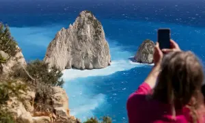 Widok na turkusowe morze Zakynthos, gdzie turystka robi zdjęcie skalistym wysepkom.