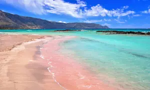 Różowa plaża na Krecie, Elafonisi, z turkusową wodą i górami w tle.