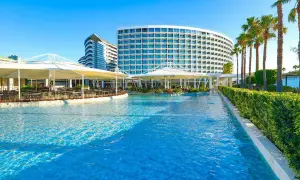 Luksusowy hotel z basenem i palmami. W oddali widać budynek w kształcie fali, a bliżej restaurację pod białymi markizami. Idealne miejsce na wypoczynek w Crystal Centro.