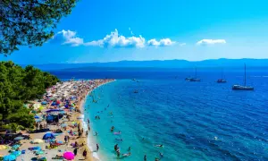 Wyspa Brać oferuje niezapomniane atrakcje: plaża Zlatni Rat tętni życiem, ludzie kąpią się w turkusowej wodzie, a żaglówki kołyszą się na morzu.