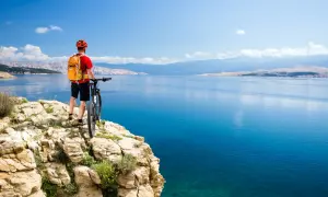 Rowerzysta na klifie podziwia widok na turkusowe morze i góry. Idealne miejsce na odkrywanie tras rowerowych Chorwacja.