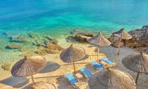 Słoneczna plaża w Ksamilu, Albania. Leżaki pod strzechą czekają na gości pakietu all inclusive.