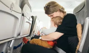 Mama tuli tulot z niemowlakiem w samolocie. Dziecko trzyma zabawkę z logo linii lotniczych.