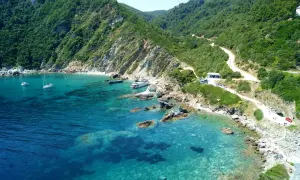 Malownicza zatoka na wyspie Skopelos z krystalicznie czystą wodą, łodziami i krętą drogą wiodącą przez zielone wzgórza.