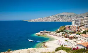 Piękna albania pogoda: błękitne morze, plaża z leżakami i hotelami na wzgórzu.