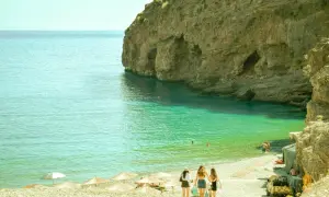 Wczesna wiosna w Grecji. Trzy dziewczyny spacerują po kamienistej plaży, woda jest krystalicznie czysta, a klify tworzą malownicze jaskinie.