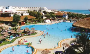 Słoneczny dzień w resorcie, ludzie kąpią się w basenie, a w tle widać morze. To idealne miejsce na wakacje w stylu caribbean world Mahdia.