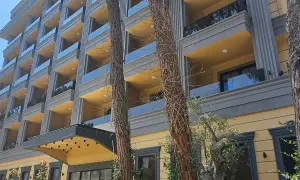 Nowoczesny hotel z żółtymi balkonami i szklanymi balustradami, otoczony drzewami. Fafa Sun Albania wita słońcem.