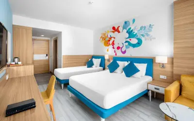 Pokój hotelowy z dwoma łóżkami i kolorową grafiką na ścianie. To jak **club sun heaven** dla podróżnych.