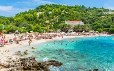 Słoneczna plaża w Chorwacji, ludzie opalają się i kąpią w krystalicznie czystej wodzie. Idealne miejsce na wakacje all inclusive samolotem.