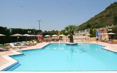 Basen hotelu Diagoras z palmą pośrodku, leżakami i parasolami.