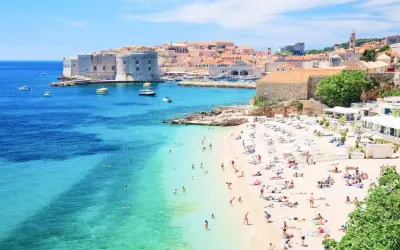 Słoneczna plaża w Dubrowniku, idealna na chorwacja last minute all inclusive. Turkusowe morze, zabytkowe mury i mnóstwo wypoczywających.