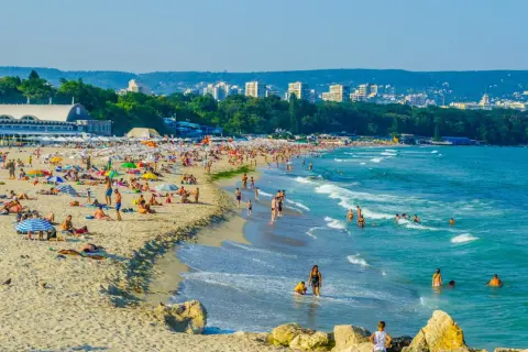Słoneczna plaża w Bułgarii, idealna na wakacje last minute all inclusive. Tłumy ludzi opalają się i kąpią w morzu.