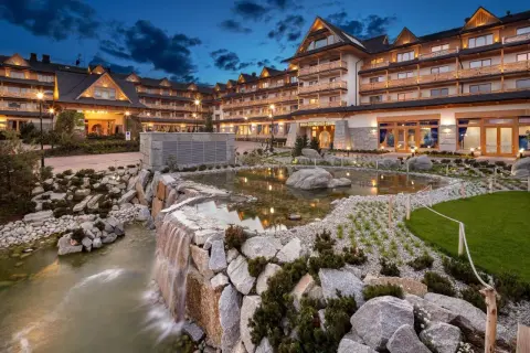 Elegancki hotel z basenami termalnymi, z kaskadą wodną i stawem w otoczeniu kamieni i zieleni.