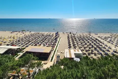 Majowa pogoda w Albanii zachwyca. Słoneczna plaża z rzędami leżaków i parasoli, turkusowe morze i błękitne niebo.