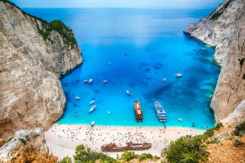 Zatoka Navagio, jedna z największych wysp greckich, z turkusową wodą, plażą pełną ludzi i wrakiem statku.