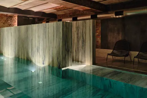 Wnętrze basenu w jednym z najlepszych hoteli spa. Marmurowe wykończenia, dyskretne oświetlenie i dwa fotele tworzą atmosferę relaksu.