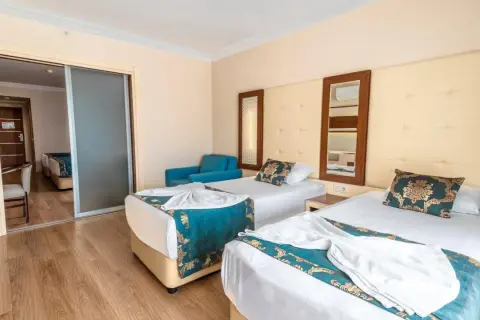 Pokój hotelowy z dwoma łóżkami, ozdobiony turkusowymi narzutami. Widok na sąsiedni pokój przez przesuwne drzwi. Idealne miejsce na relaks po dniu spędzonym w beach club doganay.