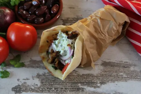Pyszny pita gyros z mięsem, warzywami i sosem, obok pomidory, oliwki i cebula.